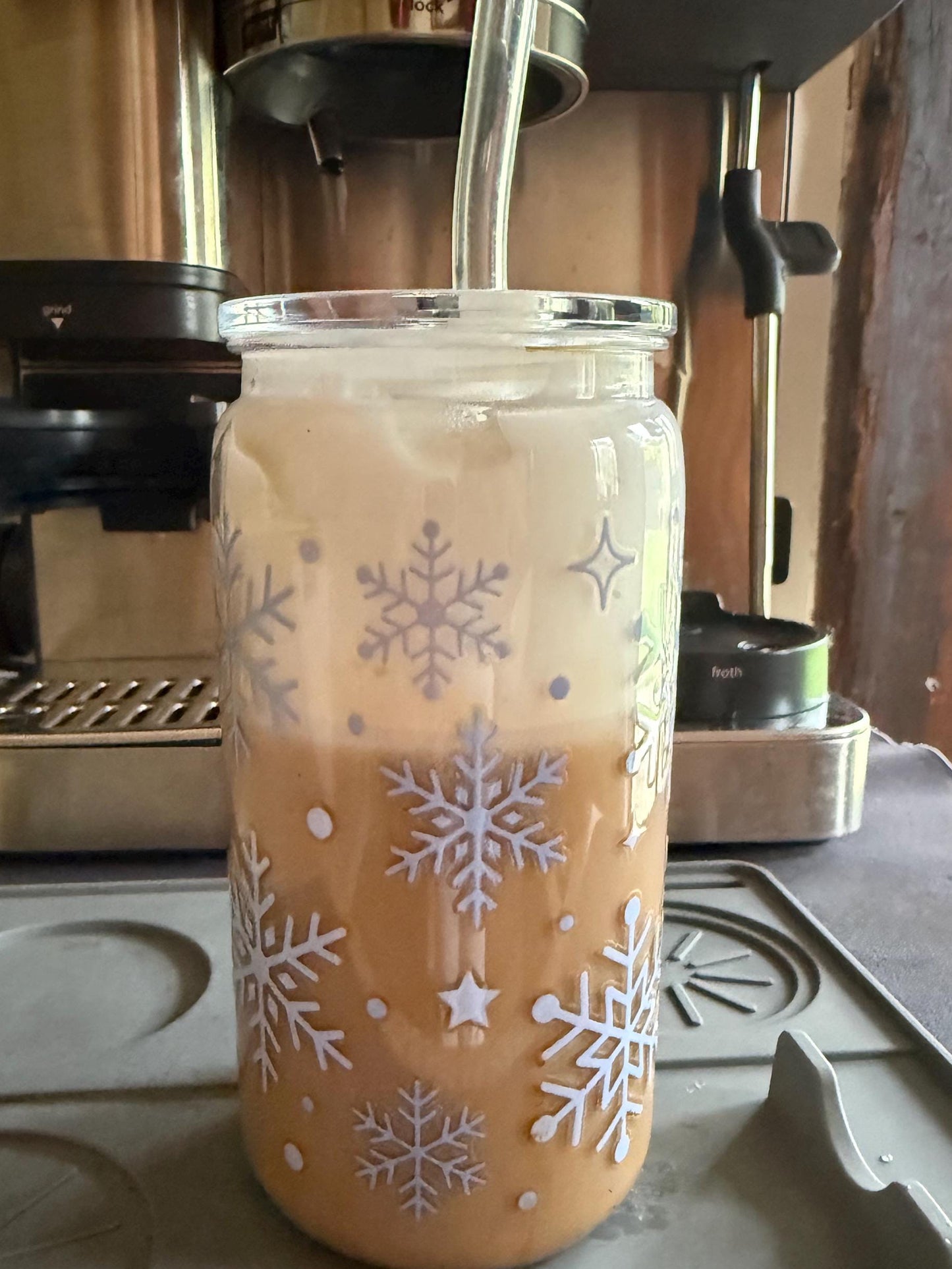 Glass mug with snowflake design filled with a creamy beverage on a stovetop.