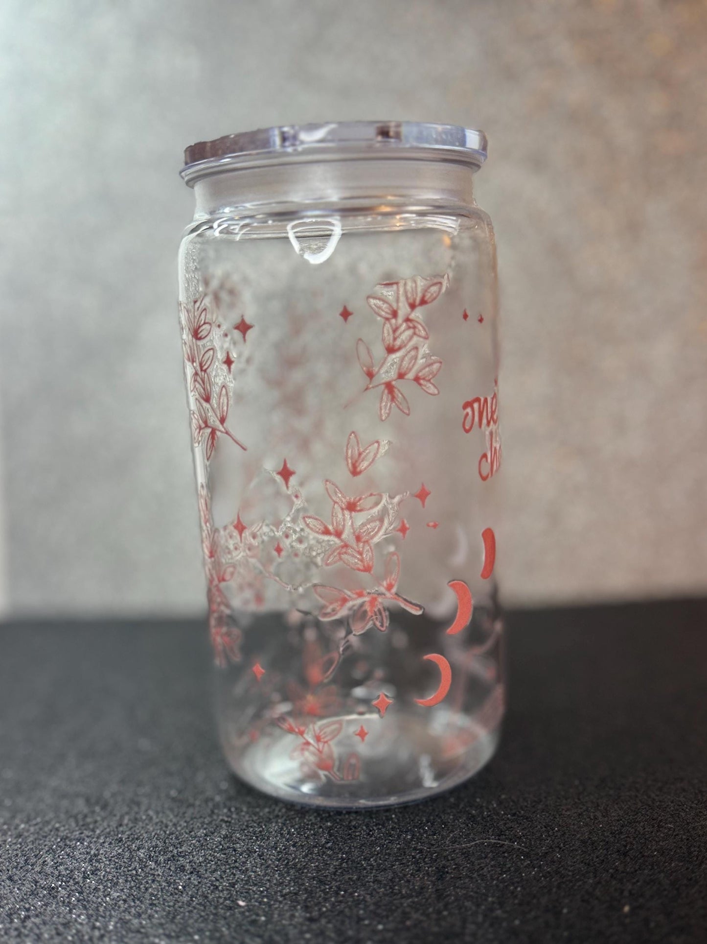 Clear glass tumbler with floral design and silver lid on a black surface
