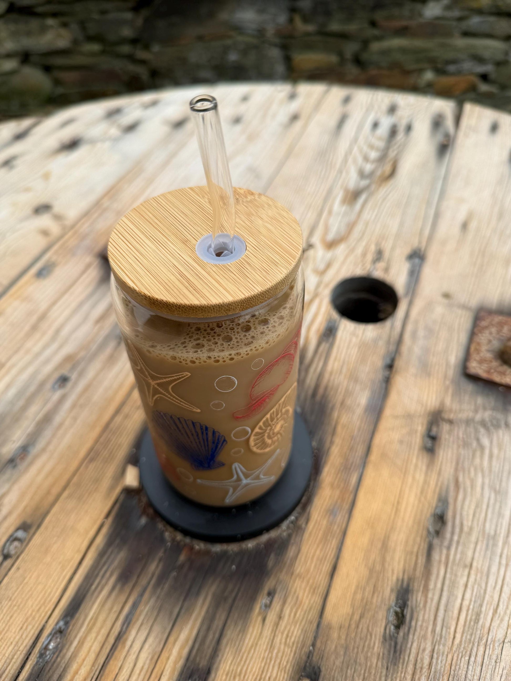 Cold brew coffee in a glass with a wooden lid and straw on a wooden surface.