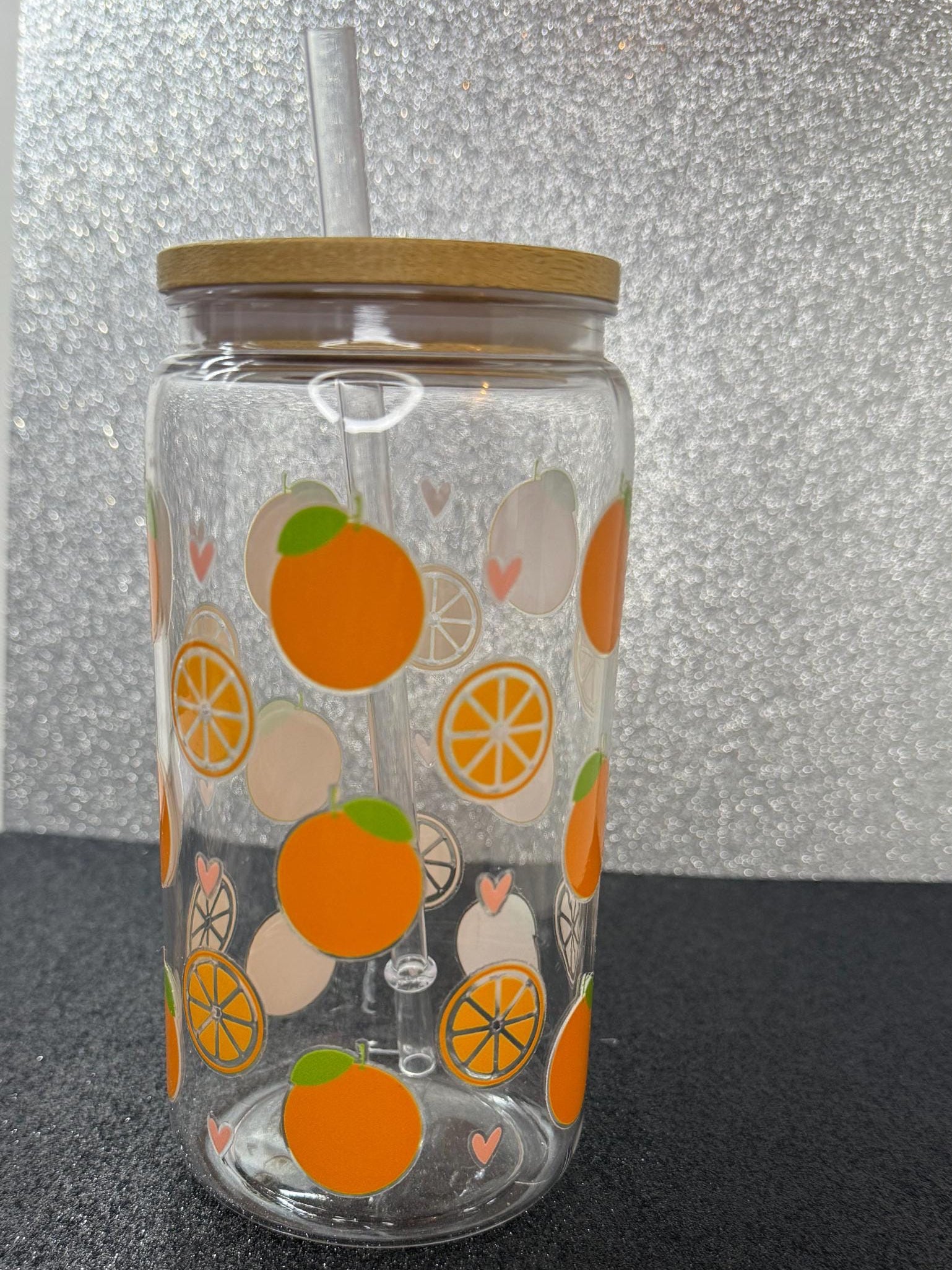 Clear tumbler with orange pattern and wooden lid on a reflective surface