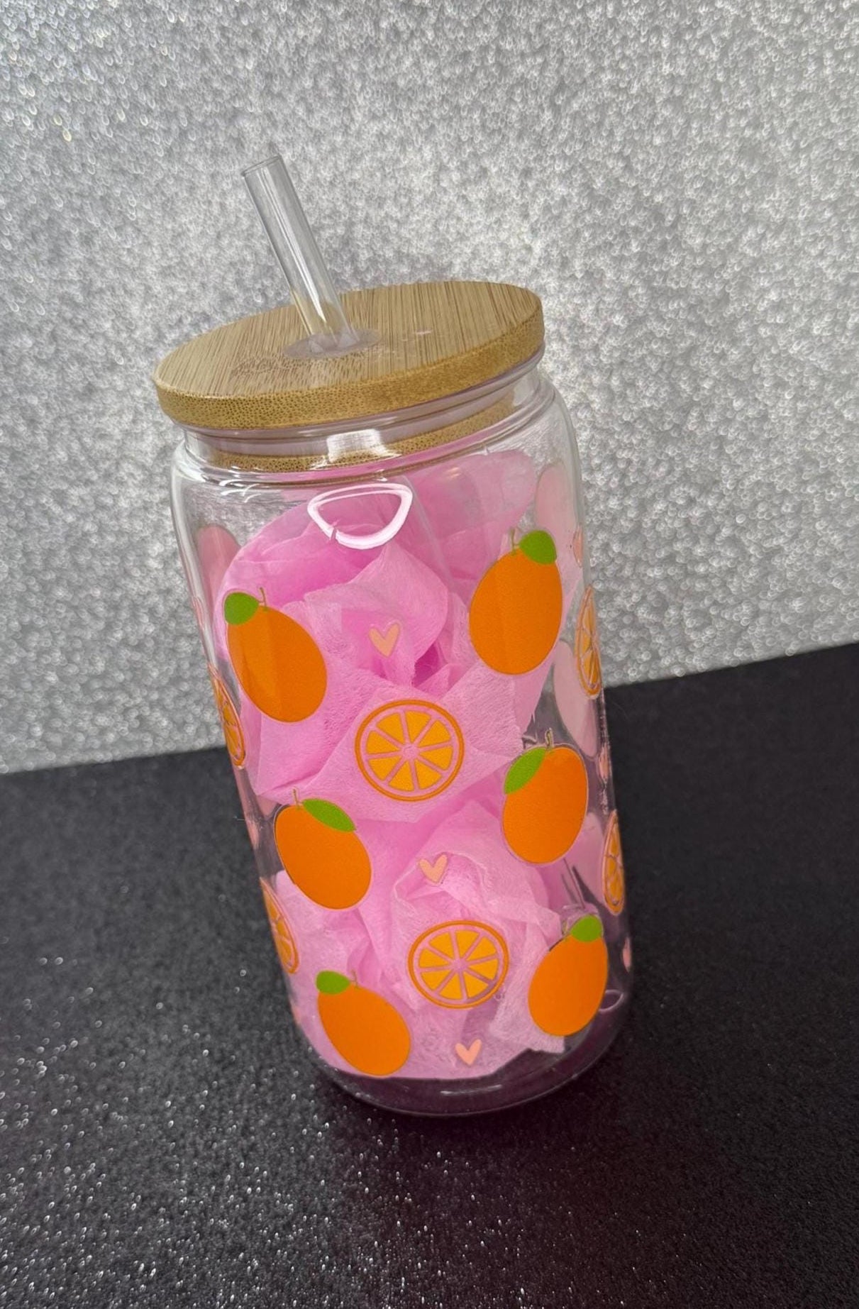Clear tumbler with pink design and wooden lid on a black surface