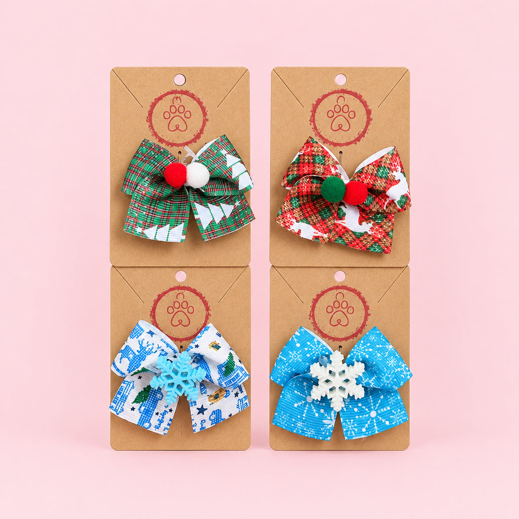 Four handmade ribbon hair bows on brown display cards, featuring green and white Christmas tree patterns, red and white plaid, blue and white snowflake patterns, and blue snowflake-patterned bows, displayed on a gray textured fabric background.
