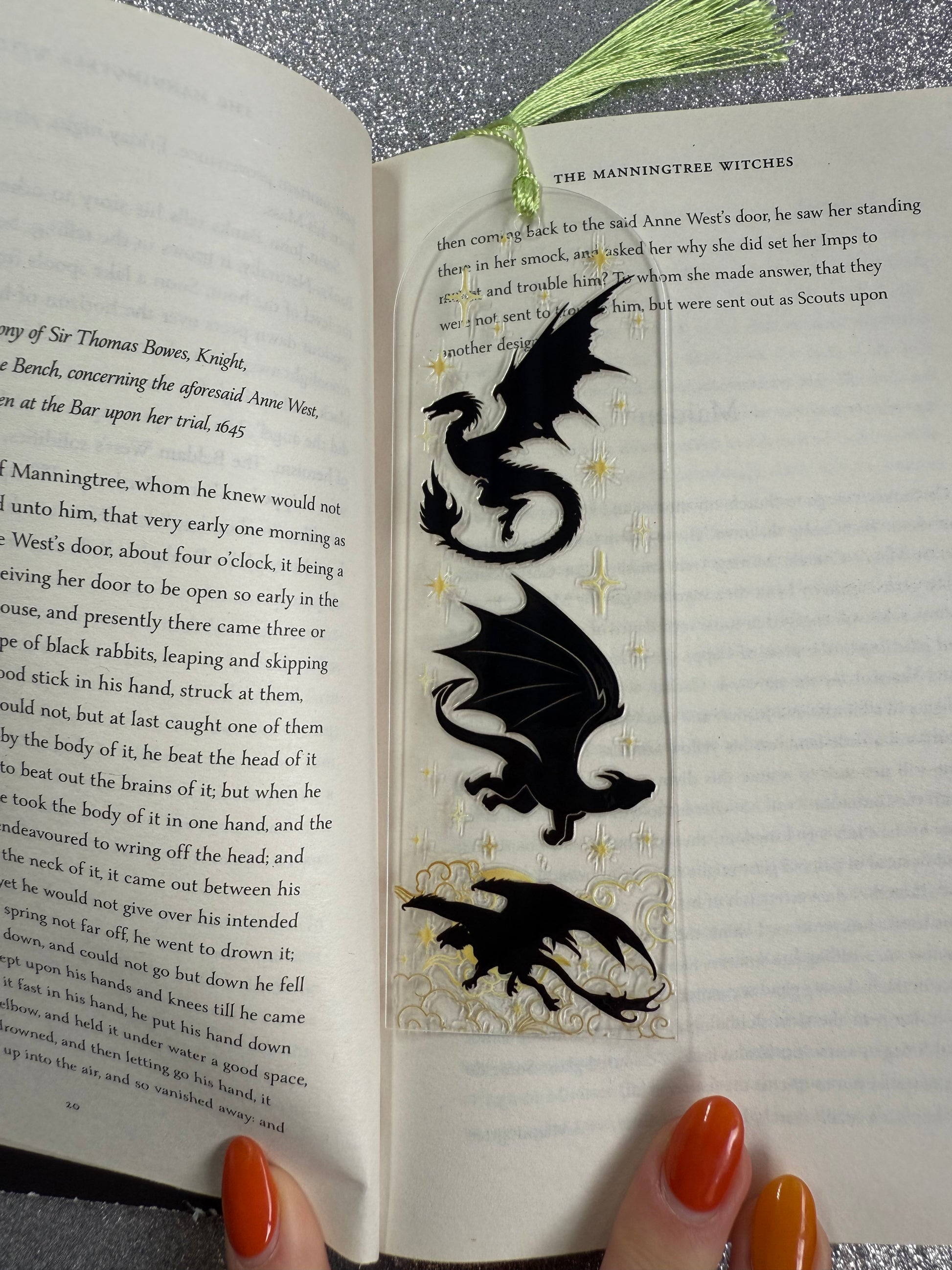 Three dragon-shaped bookmarks on an open book with a hand holding it.