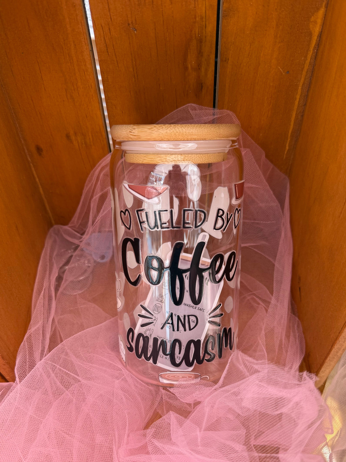 A clear glass cold cup with a light wood lid, printed with the text 'I FUELED BY Coffee AND sarcasm' in black lettering.