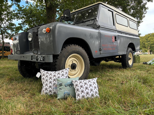 Vintage Land Rover parked outdoors with decorative pillows featuring vehicle designs.