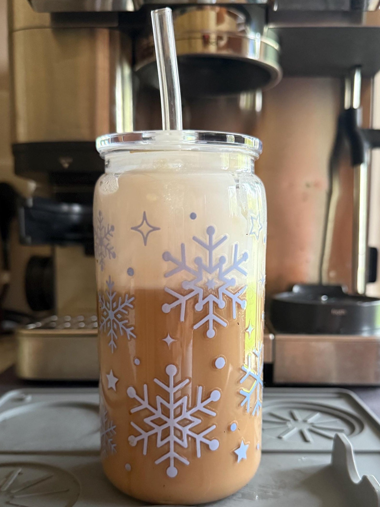 Glass jar with snowflake design filled with a creamy beverage, placed on a stovetop.