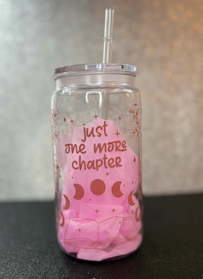 Clear tumbler with pink design and text 'just one more chapter' on a dark surface.